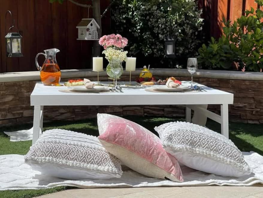 Romantic outdoor setting with a low table, pillows, a table setting with flowers and candles by Mellow Events